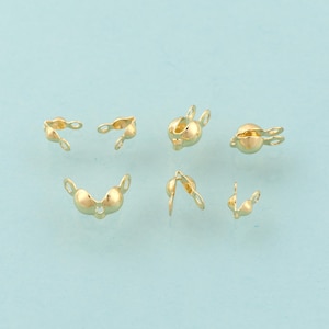 May include: Gold-colored jewelry findings, including several clasp components, are arranged against a light blue background. The findings have a rounded shape with small loops for attaching to other jewelry pieces. The components are designed for jewelry making.