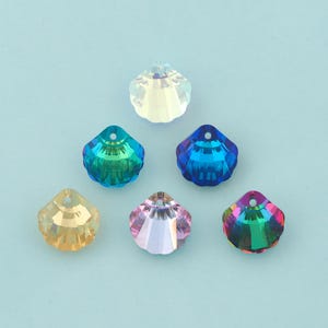 May include: Six faceted seashell-shaped beads in various colors: clear, yellow, blue, pink, and iridescent. Each bead has a hole at the top for stringing. The beads are displayed on a light blue background.