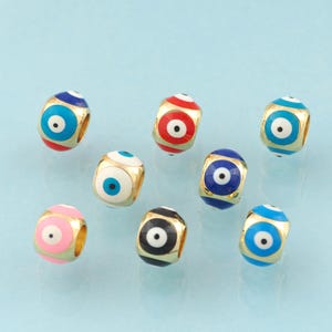 Könnte beinhalten: Acht goldfarbene Perlen mit einem bösen Auge-Design. Die Perlen sind in verschiedenen Farben, darunter blau, rot, rosa, schwarz und weiß.