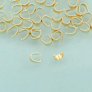 May include: A selection of small, gold-coloured jewellery findings, including open-ended U-shaped bails and half-moon shaped components. These findings are likely used for creating necklaces, bracelets, and other jewellery pieces.