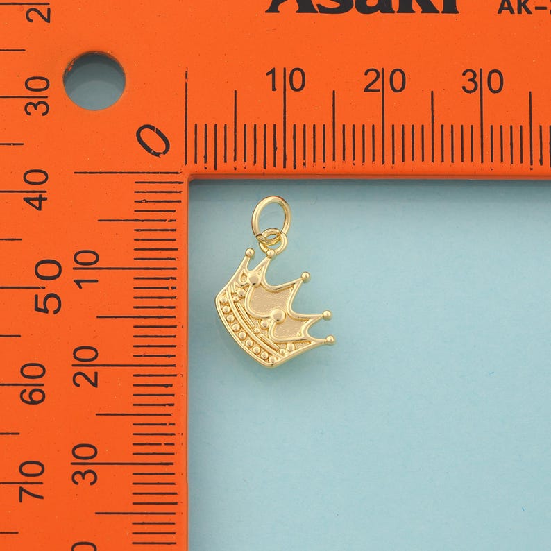 Op de afbeelding: Een goudkleurige kroonbedel met een lus aan de bovenkant om aan een ketting of armband te bevestigen. De kroon heeft een gedetailleerd ontwerp met kleine ronde accenten en drie prominente punten. De bedel is ongeveer 1,3 cm hoog.