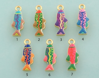 Op de afbeelding: Zeven goudkleurige metalen visbedels met kleurrijke emaille details. Elke bedel heeft een unieke kleurencombinatie, waaronder blauwe, groene, paarse, roze en oranje patronen. Elke vis heeft een klein rond oogje aan de bovenkant om op te hangen.