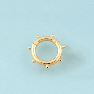 May include: Gold-toned metal ring with a circular design and small decorative balls around the edge.