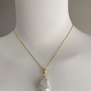 Könnte beinhalten: Eine goldene Kettenkette mit einem großen, weißen Barockperlenanhänger.