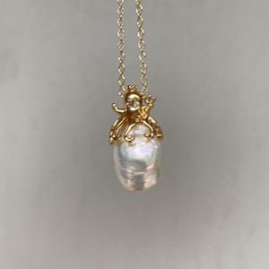 May include: A gold necklace with a large, white baroque pearl pendant. The pearl is topped with a gold octopus charm with a small diamond accent.