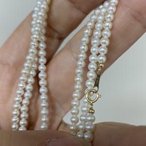 Puede incluir: Un collar de perlas blancas con un cierre de oro. El cierre está marcado con el texto "K18."