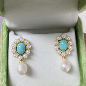 May include: A pair of gold earrings with turquoise stones and pearl drops. The earrings are in a green velvet box.