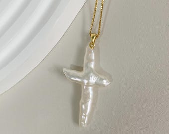 May include: A gold chain necklace with a white pearl cross pendant.