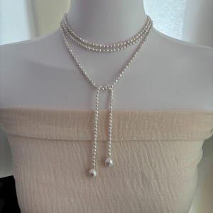 Może przedstawiać: Srebrny naszyjnik z pereł z długą, zwisającą perłą na końcu każdego sznura.