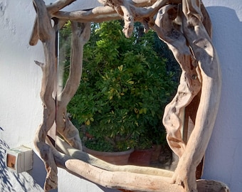 May include: A rustic mirror with a frame made of natural driftwood branches. The mirror reflects a green leafy tree in the background.