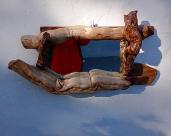 May include: A wooden mirror with a rustic design. The mirror is framed by branches of wood that have been carved into a unique shape. The mirror is hanging on a white wall.