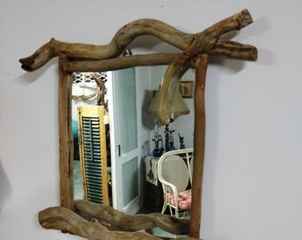 May include: A rustic wooden mirror with a unique, natural branch frame. The mirror reflects a room with a white chair and a lamp.