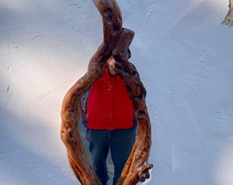 May include: A wooden mirror with a unique, natural design. The mirror is shaped like a twisted branch, with a smooth, reflective surface. The wood is a rich brown color, with knots and grain patterns visible.