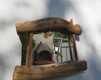 May include: A rustic, wooden-framed mirror with a natural, unfinished look. The frame is made from thick, weathered branches, giving it a unique, organic aesthetic. The mirror reflects an outdoor scene with a brick barbecue and a ladder.