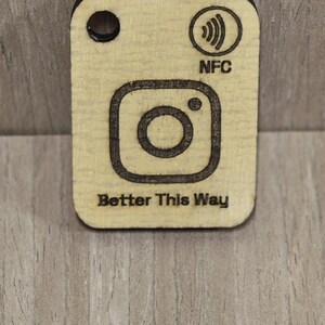May include: Wooden NFC tag with an Instagram logo and the text "Better This Way". The tag also features a small black dot and the word "NFC".