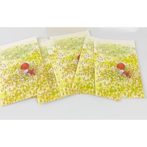 May include: A set of six blank cards with a watercolor illustration of a person in a red hat and a red dress lying in a field of white flowers.