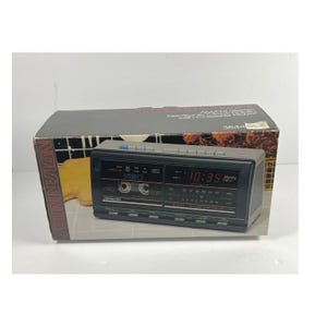 May include: A black AM/FM stereo radio with a cassette player, displayed in its original box. The radio has a digital clock display showing 10:35. The box has the brand name "SOUNDESIGN" printed on the side.