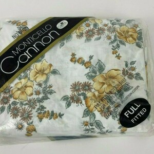 May include: A white fitted sheet with a floral pattern in shades of yellow, brown, and green. The sheet is packaged in plastic and labeled "No-Iron Monticello Cannon Full Fitted Bottom Sheet for 54 x 76 in Mattress, 65% Polyester 35% Cotton (Coton)".