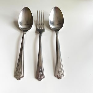 May include: Three pieces of vintage silverware: two spoons and a fork. The spoons have oval bowls and long, tapered handles with a decorative design. The fork has four tines and a matching handle. All pieces are made of a shiny, silver-colored metal.