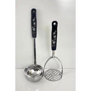 May include: A stainless steel ladle and potato masher set. The black handles feature a white starburst design. The ladle has a round bowl, and the masher has a slotted head.