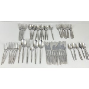 May include: A collection of stainless steel silverware, including forks, spoons, knives, and butter knives. The silverware has a floral design on the handles and is arranged on a white surface. The set includes various sizes of spoons and forks.