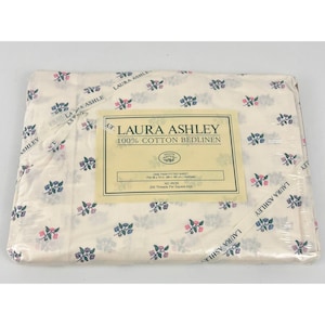 May include: A packaged Laura Ashley twin fitted sheet. The sheet is white with a floral pattern in blue and pink. The packaging includes a label with the Laura Ashley logo and product information.