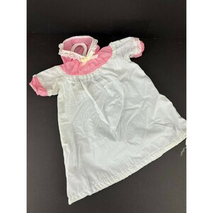 May include: A white doll dress with pink and white gingham trim and white lace. The dress has short sleeves and a gathered neckline.
