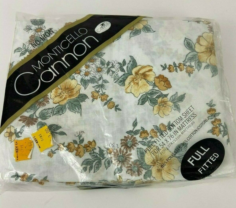 May include: A white fitted sheet with a floral pattern in shades of yellow, brown, and green. The sheet is packaged in plastic and labeled "FULL FITTED" for a 54 x 76 inch mattress. The label also states "MONTICELLO Cannon" and "65% POLYESTER 36% COTTON (COTON)".
