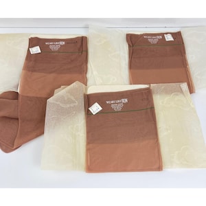 May include: Several pairs of vintage nylon stockings in shades of brown, packaged with tissue paper. The packaging reads "WEARS LIKE IRON". The stockings are displayed on a white surface.