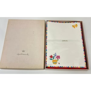 May include: A vintage Hallmark stationery set in a beige box. The box contains white stationery with colorful floral and butterfly designs. The edges of the stationery are trimmed with a colorful zig-zag pattern. The Hallmark logo is visible on the box and stationery.