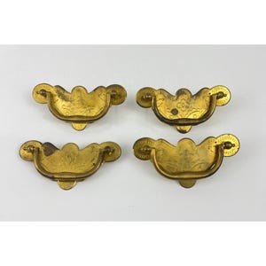 May include: Four antique brass drawer pulls with a floral design. Each pull has a curved handle and decorative circular ends. The brass has a slightly aged appearance, suggesting vintage or antique status. These pulls are suitable for furniture restoration or decorative projects.