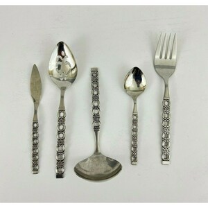 May include: Set of five silver-toned flatware pieces with ornate handles. The set includes a butter knife, a slotted spoon, a serving spoon, a fork, and a ladle.