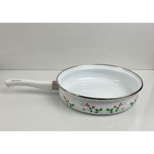 May include: White enamel frying pan with a white handle and silver rim. The pan features a floral design with red berries and green leaves around the base. The pan is designed for cooking.