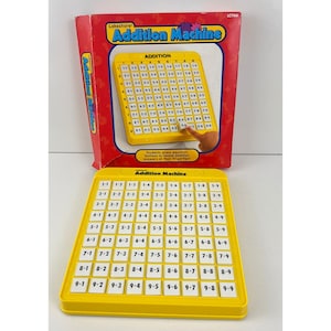 Pode incluir: Um brinquedo educativo amarelo Lakeshore Addition Machine com uma caixa vermelha. A máquina tem uma grade de botões para problemas de adição. A caixa diz: "Os alunos pressionam os botões da equação para revelar as respostas de adição ao seu alcance!"