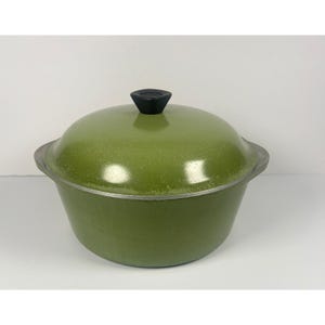 May include: A round, olive green cooking pot with a matching lid and a black knob handle. The pot features integrated side handles and a metallic rim, showcasing a smooth, glossy finish on the exterior surface of the cookware vessel.
