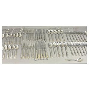 May include: A large collection of silver-toned stainless steel flatware, including numerous dinner forks, salad forks, dinner knives, and various sizes of spoons. The utensils feature a simple, polished finish with a classic handle design.