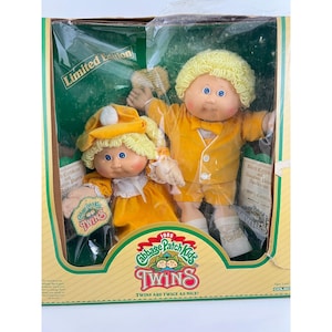 May include: A vintage 1985 Cabbage Patch Kids Twins set in its original packaging. The dolls have yellow curly hair, blue eyes, and wear matching yellow outfits. The box features the words "Limited Edition" and "Twins are twice as nice!"