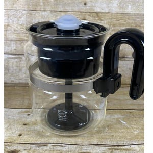 May include: A clear glass coffee maker with a black filter and handle. The coffee maker has a silver band and a black lid with a light blue top. The text "SCHOTT DURAN Germany" is visible on the glass.