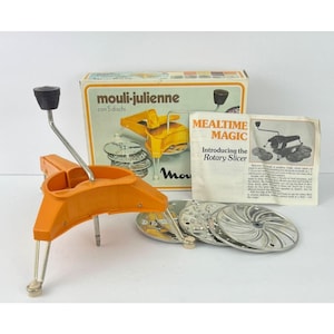 May include: An orange Mouli-Julienne rotary slicer with five discs, a black handle, and a silver crank. The box reads "Mouli-Julienne con 5 dischi" and "Mealtime Magic Introducing the Rotary Slicer". The slicer is a vintage kitchen tool.