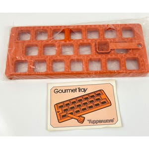 May include: An orange plastic ice cube tray with a matching scoop, still in its original packaging. The tray has 21 square compartments. A printed card with the words "Gourmet Tray" and a diagram of the tray is also visible.