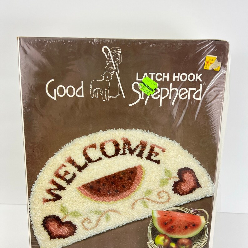 May include: A latch hook kit featuring a welcome mat with a watermelon design. The kit includes a brown background with the words "Good Shepherd" and "Latch Hook" printed on it. The kit is packaged in plastic.