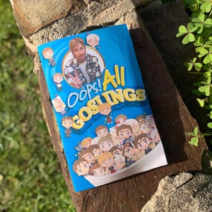 May include: A rectangular blue cereal box with the text Oops! All GOSLINGS printed in yellow. The design features a circular portrait of a man in a plaid shirt and numerous small, cartoon-style illustrations of the same man in various outfits.