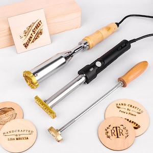 May include: Three metal branding irons with wooden handles and electrical cords, alongside several circular wooden discs featuring burned designs including "Regent Street," "Handcrafted by Lisa Meccia," and "Hand Crafted by Pete's Place."