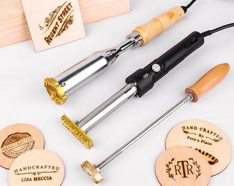 Könnte beinhalten: Drei Metall-Brennstempel mit Holzgriffen und Stromkabeln, zusammen mit mehreren runden Holzscheiben, die eingebrannte Motive wie "Regent Street", "Handcrafted by Lisa Meccia" und "Hand Crafted by Pete's Place" aufweisen.