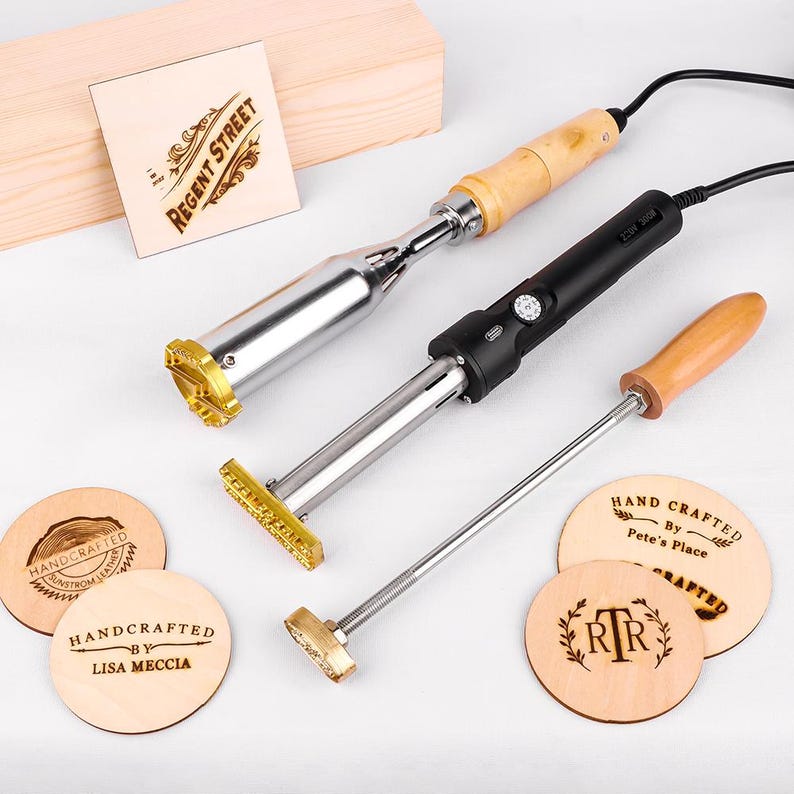 May include: Three metal branding irons with wooden handles and electrical cords, alongside several circular wooden discs featuring burned designs including "Regent Street," "Handcrafted by Lisa Meccia," and "Hand Crafted by Pete's Place."