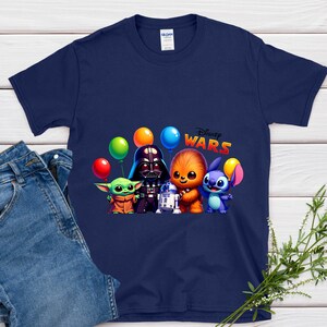 May include: Navy blue t-shirt with a colourful graphic of Star Wars characters, including Darth Vader, Chewbacca, and Stitch, holding balloons. The words "Disney Wars" are printed in a playful font. The shirt is paired with blue jeans.