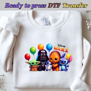 May include: White sweatshirt with a colourful graphic of Star Wars characters, including Darth Vader, Chewbacca, and Stitch, with balloons. The text "Disney Wars" is also displayed. The words "Ready to press DTF Transfer" are at the top.