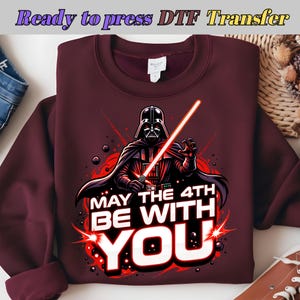 Puede incluir: Sudadera burdeos con un gráfico de Darth Vader sosteniendo un sable de luz rojo. El texto "MAY THE 4TH BE WITH YOU" está en blanco y rojo. La parte superior dice "Ready to press DTF Transfer".