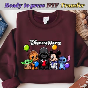 May include: Burgundy sweatshirt featuring a graphic of Disney characters, including Yoda, Chewbacca, Darth Vader, Mickey Mouse, and Stitch. The text "Disney Wars" is above the characters. The words "Ready to press DTF Transfer" are at the top.