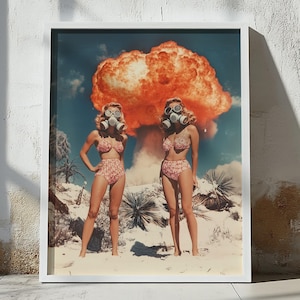 May include: A framed print depicting two women in matching floral bikinis and gas masks, set against a backdrop of a desert landscape and a large orange explosion. The artwork has a retro, vintage aesthetic.